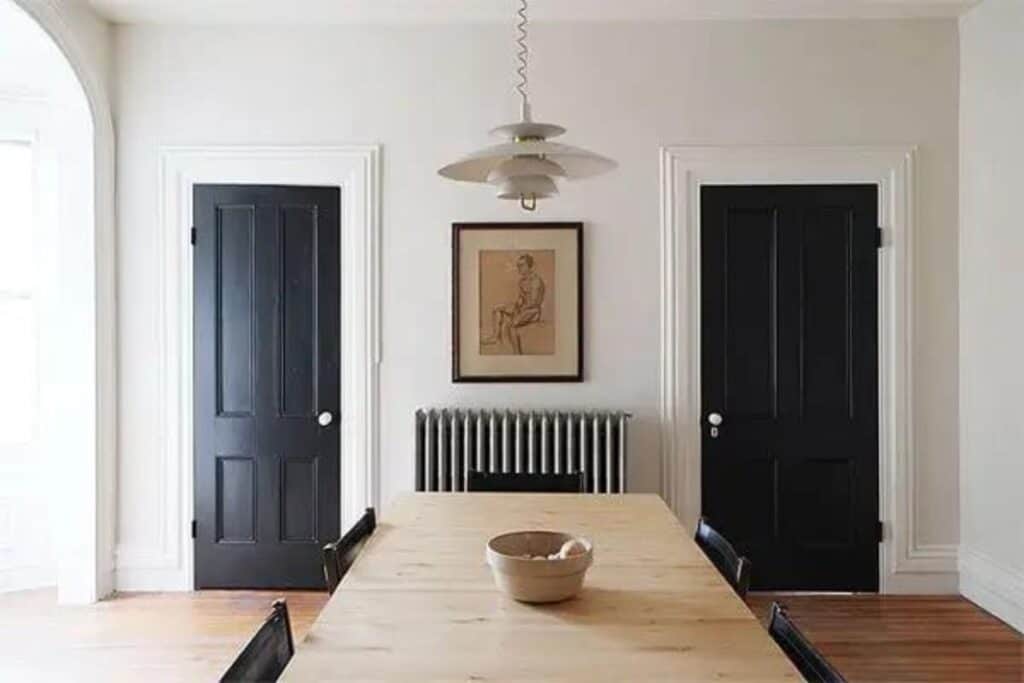 A dining room with black doors, white trim and a light wood table.