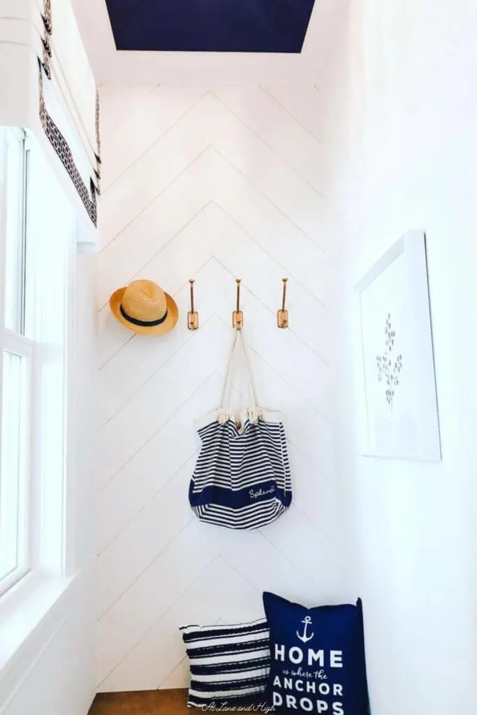 A chevron shiplap accent wall painted white with a dark blue ceiling, a bench and nautical accents.