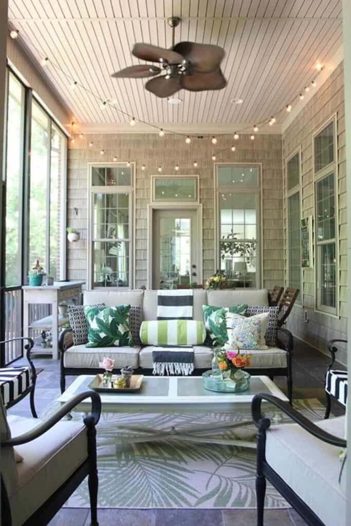 A screened in porch with dark furniture and light gray cushions, a white coffee table and lots of pillows on the couch.