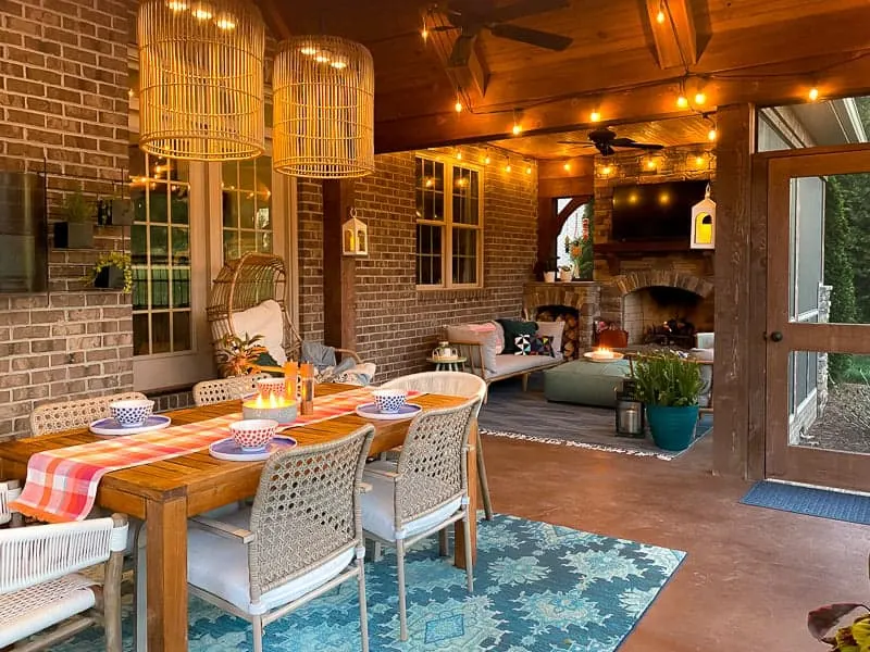 A screened in porch with a fireplace, string lights and a dining table.