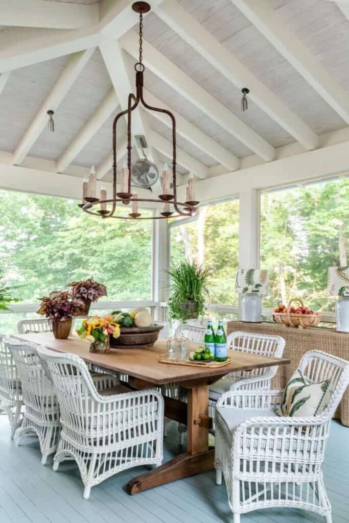 A screened in porch with a wood dining table and white wicker chairs.