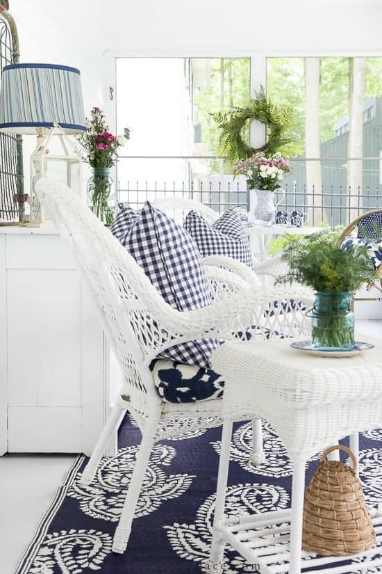 A screened in porch with white wicker furniture and blue and white checkered pillows.