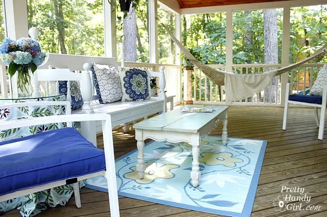 A screened in porch with a white wood bench, a chair with a royal blue cushion and a hammock.