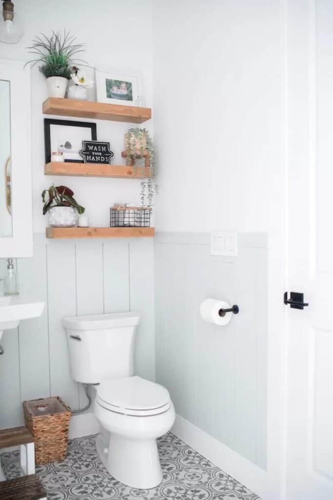 Vertical shiplap painted a light blue-green in a bathroom with white on the walls above and two wood shelves above the toilet.