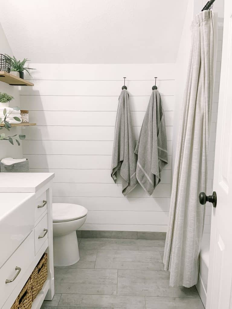 White shiplap in a bathroom with two towel hooks with gray towels hanging from them and a light gray shower curtain.