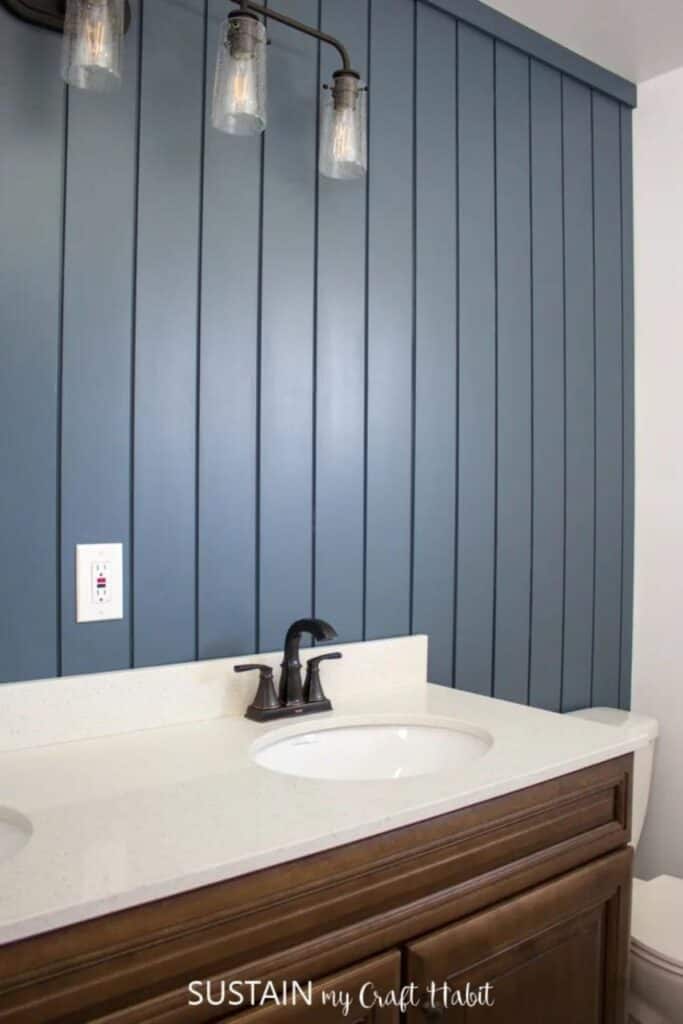 Dark blue gray painted shiplap hung vertically in a bathroom with a wood vanity and beige counter.