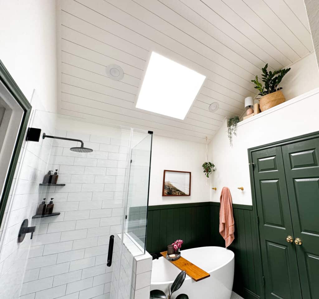 A bathroom with shiplap on the ceiling painted white and shiplap on the walls halfway up painted dark green as well as the doors.