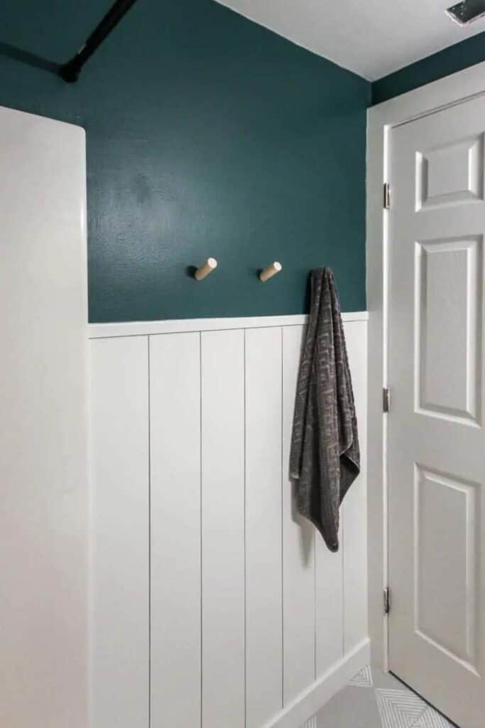 White vertical shiplap halfway up the wall with teal painted above and a gray towel hanging on hooks.