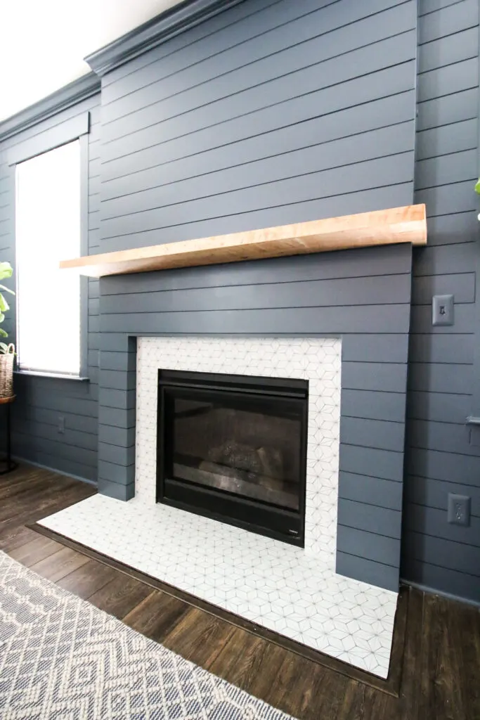 A fireplace with navy blue painted shiplap and a wood mantel.