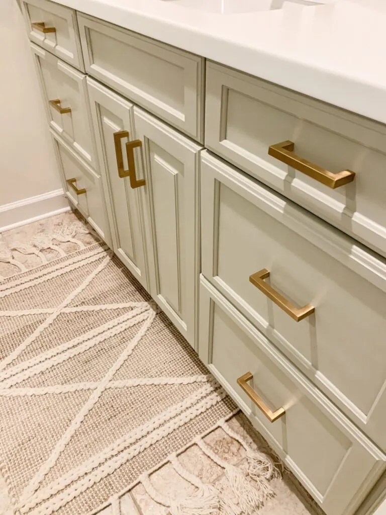 A bathroom vanity painted in Jogging Path with gold hardware and a white counter.