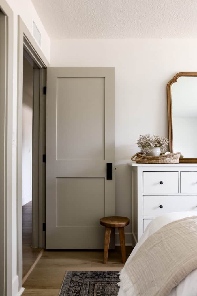 Sherwin Williams Jogging Path on the doors and trim of a bedroom with a white dresser and a small wood stool in front of the door.