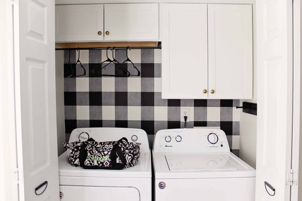 A laundry room with black and white plaid wall paper behind the mchaines.