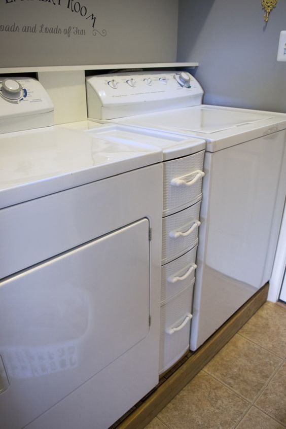 A laundry room with white plastic drawers in between the machines.