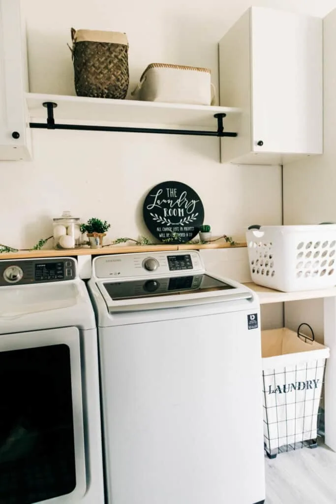 A laundry room with cream walls, a shelf above the washer and dryer and a basket on a shelf to the right of the machines.