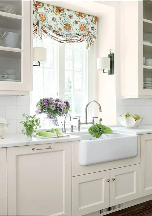 Linen White on cabinets with silver hardware, a white farmhouse sink with a window above and lots of pretty flowers.