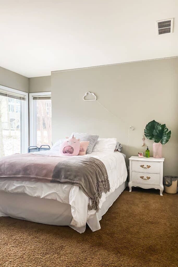 A bed with white bedding and pink throw pillows, a cloud led light above and a white nightstand.