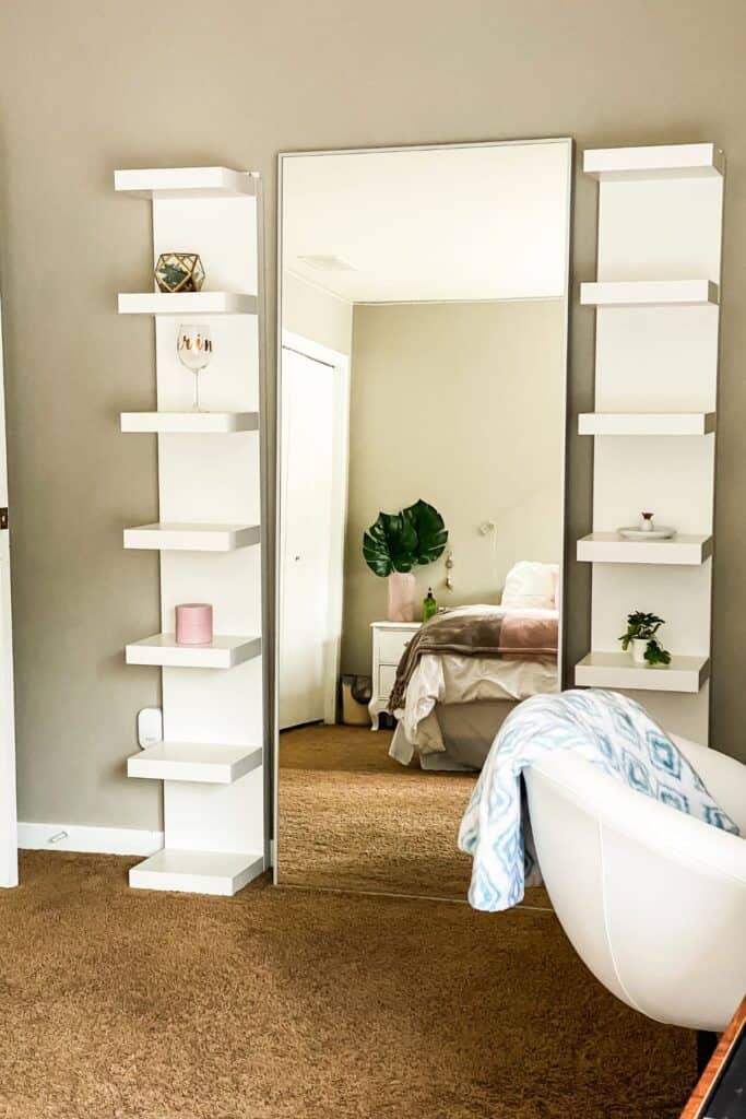A large mirror leaning on a wall with shelves on either side and brown carpet.