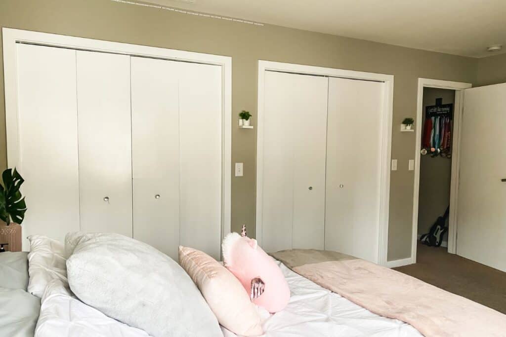Gray/brown walls and two sets of closet doors on one side of a bedroom.
