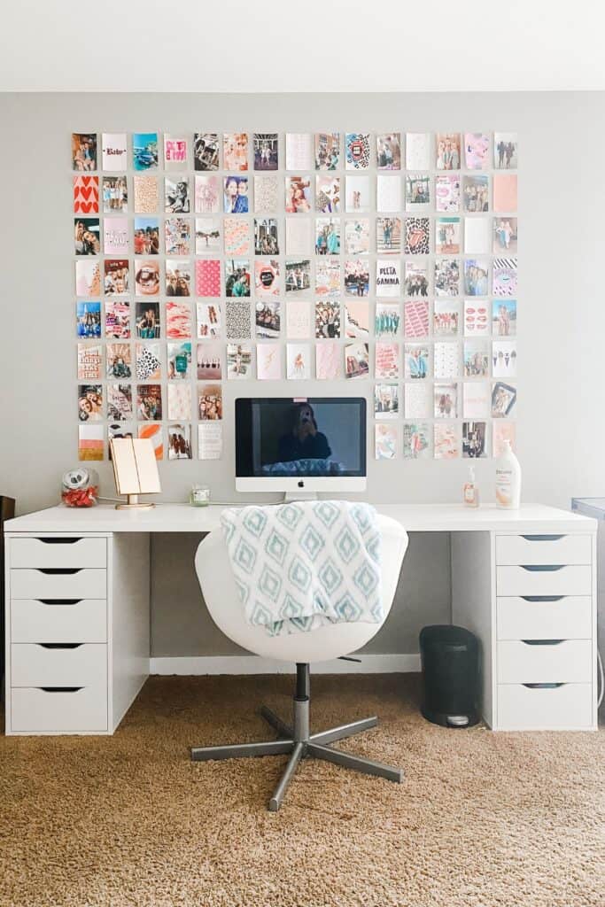 A desk with a computer on it and a grid of photos on the wall all around the computer.  
