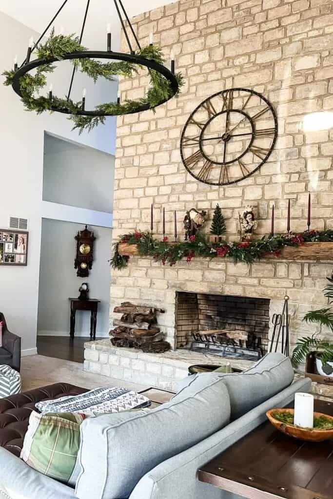 The family room with a large stone fireplace, a wagon wheel chandelier with garland on it and a table in the distance with a german clock above.
