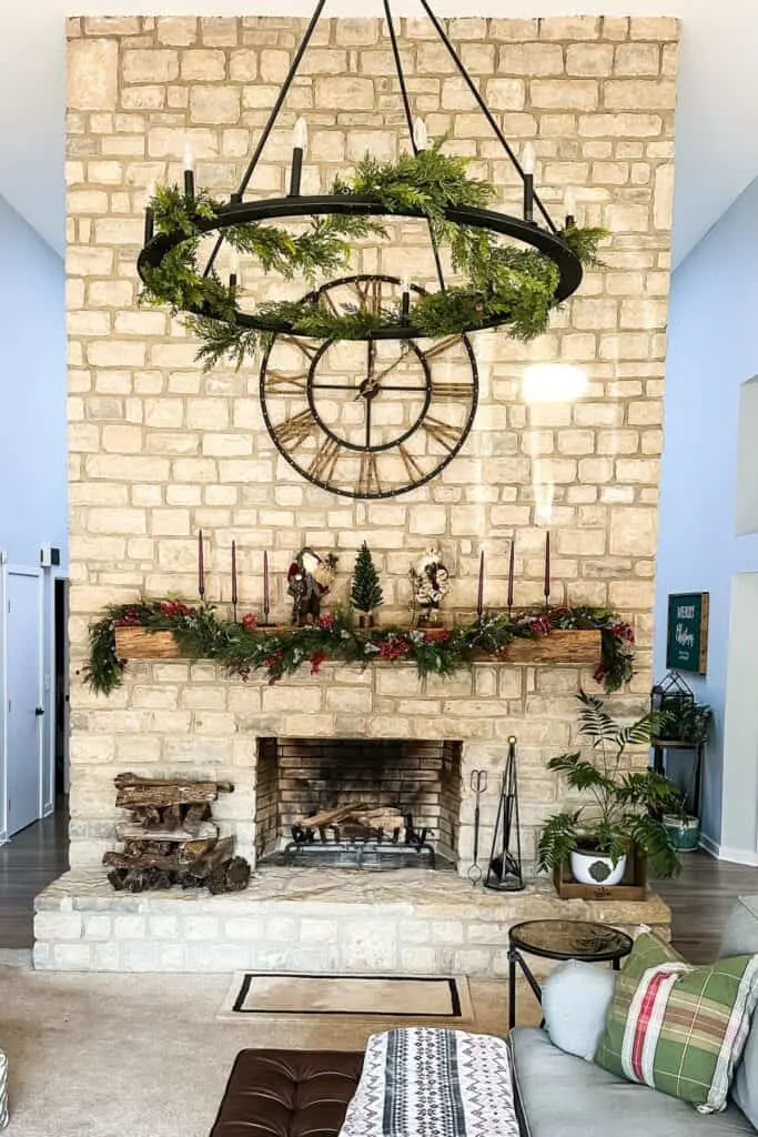 a fireplace with a large beam mantel and a strand of garland on it, three candles on each side with two santas and a small christmas tree in the center.
