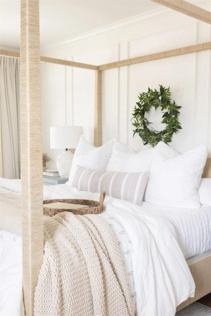 Walls painted in Cloud White with picture molding, a green wreath on the head board wall with a four poster bed that has been wrapped in twine.