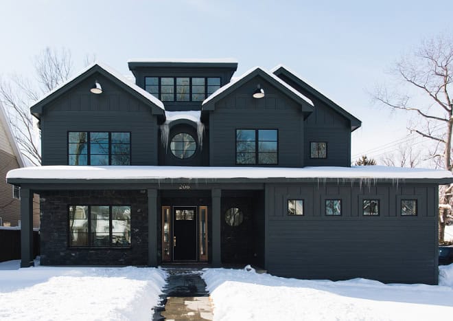 A black house with black trim set in winter with snow on the ground, on the roof, and icicles hanging from the gutters.
