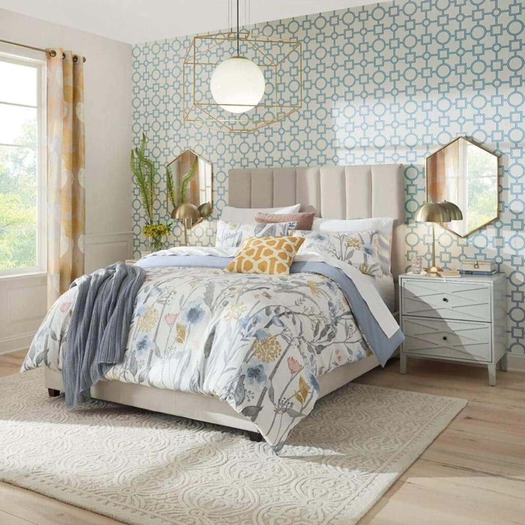 A bedroom with the headboard wall decorated in wallpaper with a blue geometric design and floral bedding.