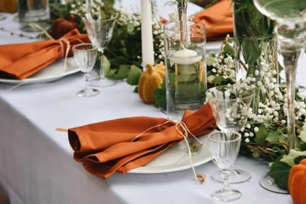 A fal table setting with lots of greenery, babys breath, and white plates with dark orange napkins.