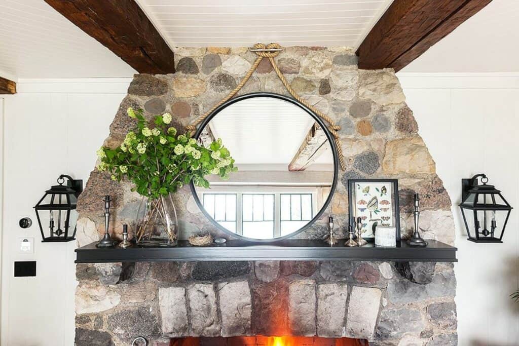 A stone fireplace with black sconces flanking it and a round mirror on a black mantel.