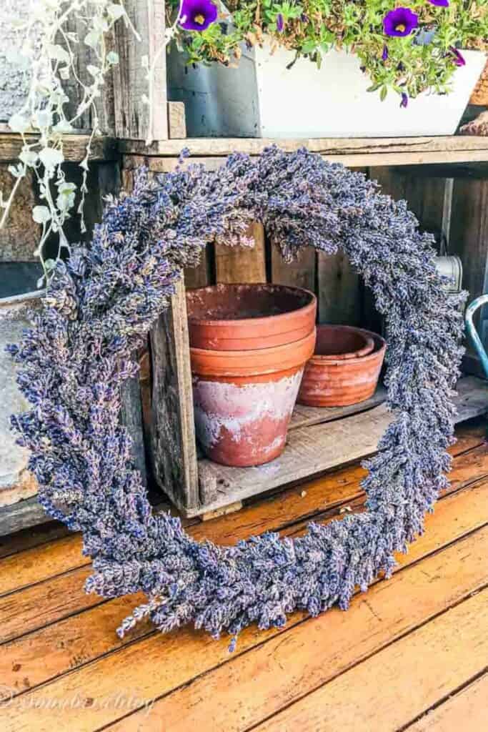 A lavender wreath leaning up against a potting table with a white tub and terra cotta pots on a wooden floor.