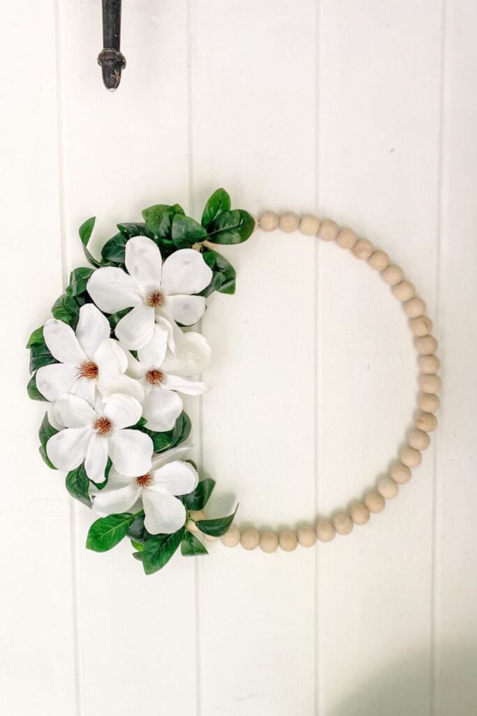 A bead ornament with magnolia flowers on the left side hanging on a vertical shiplap wall. 