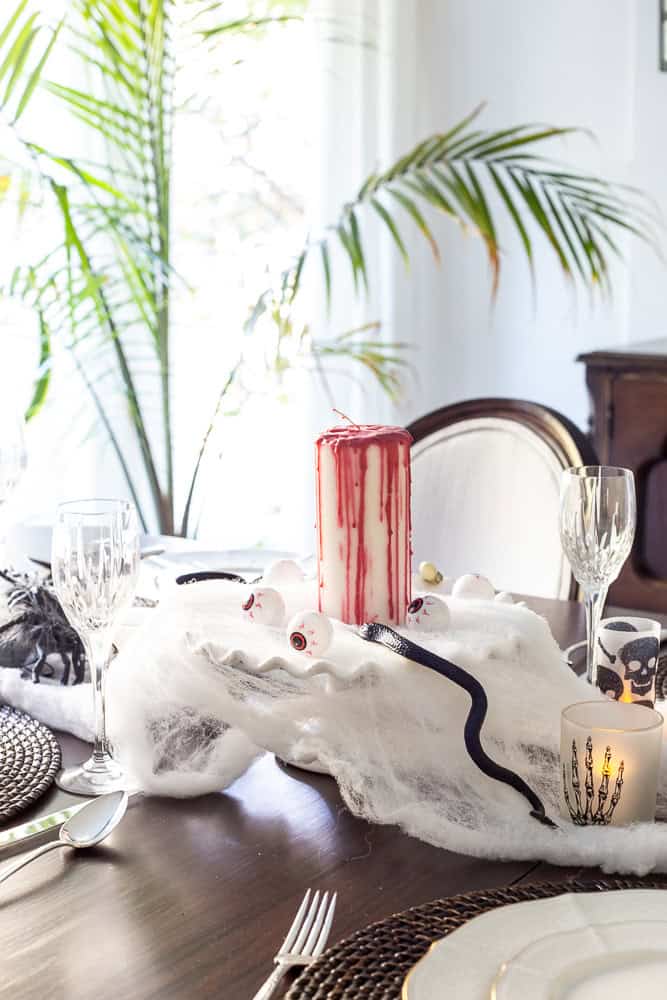 A view of my halloween centerpiece with a cake stand and candle with what looks like blood dripping down it, snakes climbing up and eyeballs surrounding the candle.