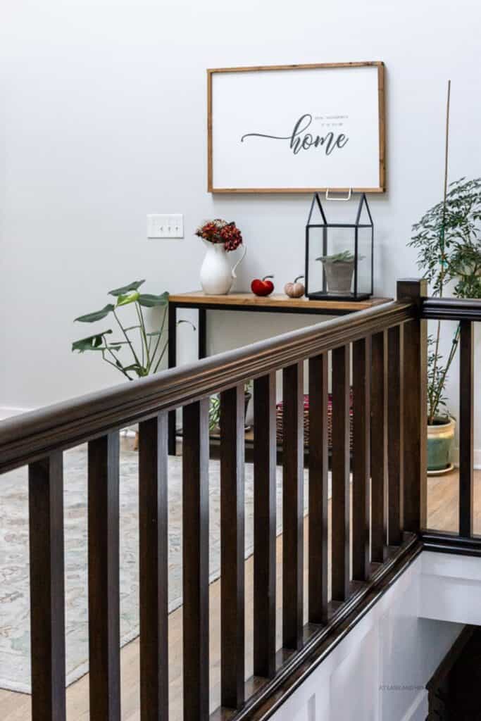 A view of my entryway with the stairwell in the foreground and the entry table in the background with a white vase of flowers, two pumpkins and a lantern with a plant inside it.