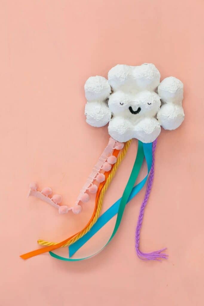 A cloud made out of an egg carton and streaming tales that look like a rainbow using different fabric.