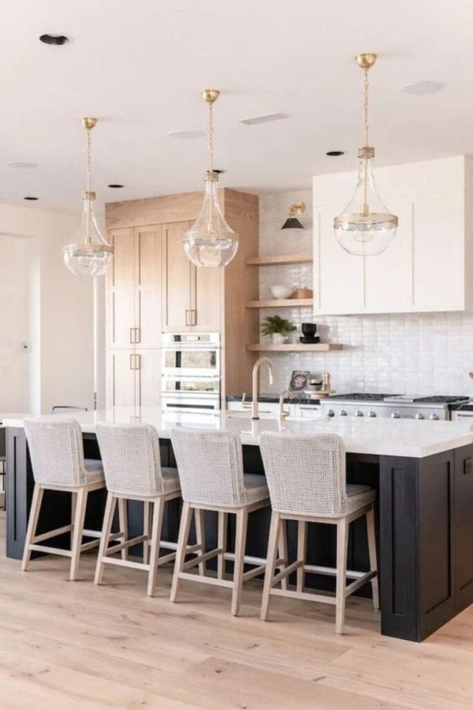 A kitchen with white and wood perimeter cabinets and a black island with white counters and four barstools.