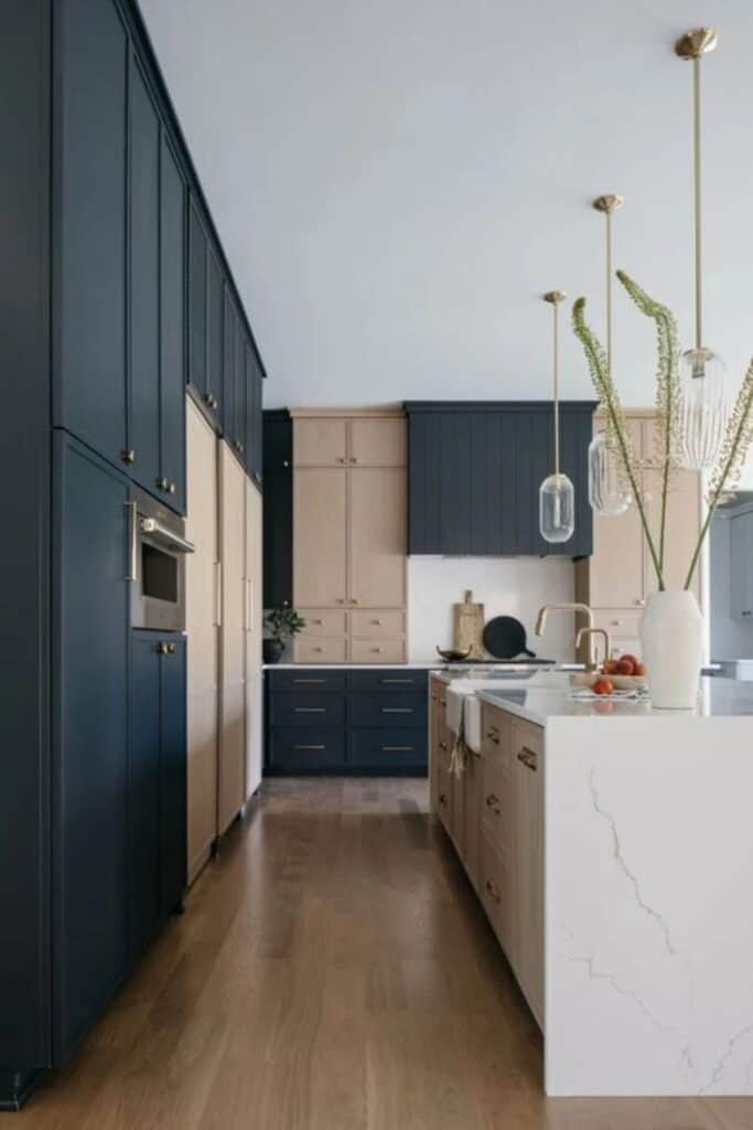 Two tone cabinets in a kitchen with black and beige cabinets with marble counters and wood floors.