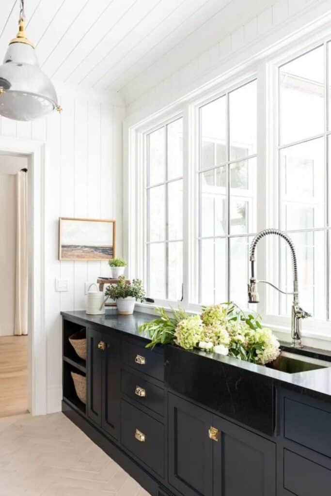 Black cabinets under a wall of windows and flowers in the sink with silver hardware.