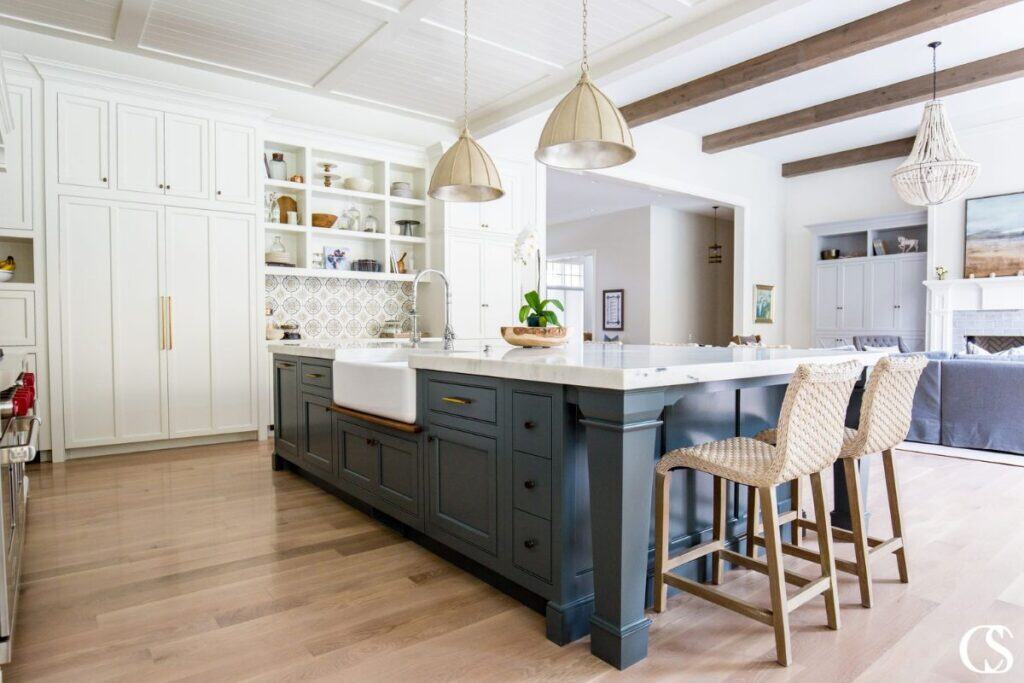 A kitchen with white perimeter cabinets, a blue island and white counters, with wood floors.