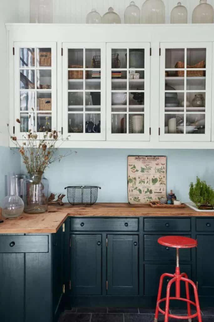 Dark blue lower cabinets with a wooden counter and white upper cabinets and a red antique stool.