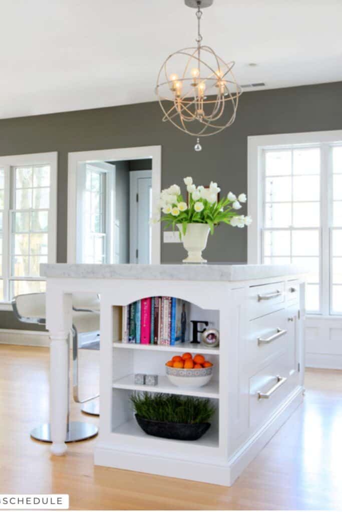 A kitchen with Chelsea Gray on the walls, lots of windows with white trim, white cabinets and marble counters.