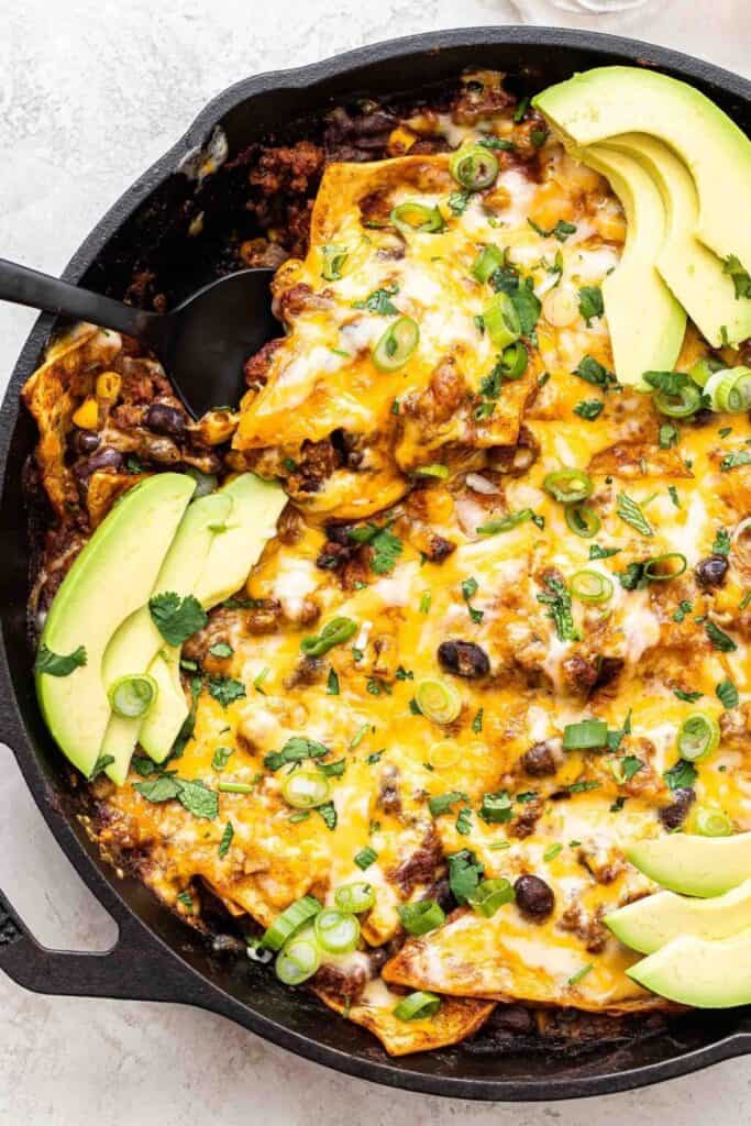 Beef Enchiladas in a cast iron skillet with avacados and scallions topping it.