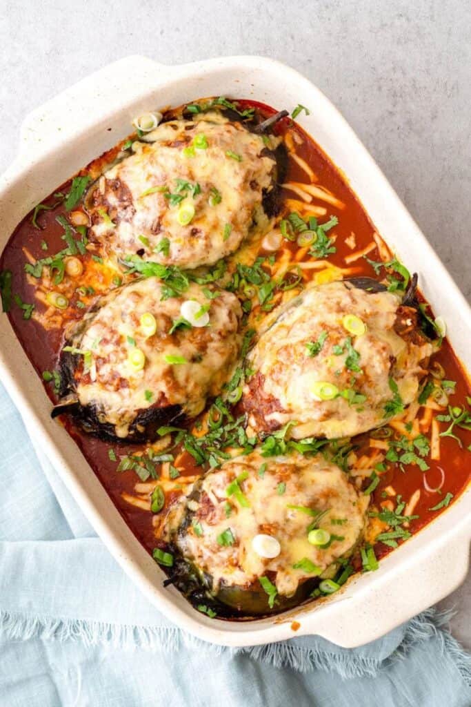 Stuffed Poblano peppers in a white baking dish on a gray counter with a blue towel.