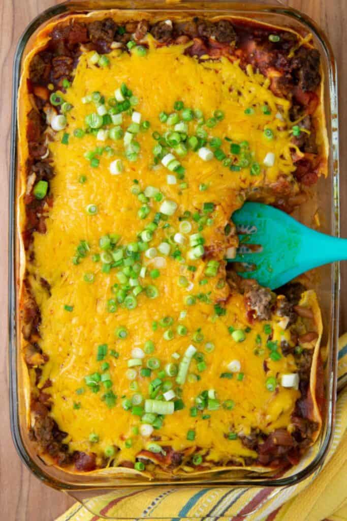 Beef enchiladas on a glass baking dish with a blue spatual.