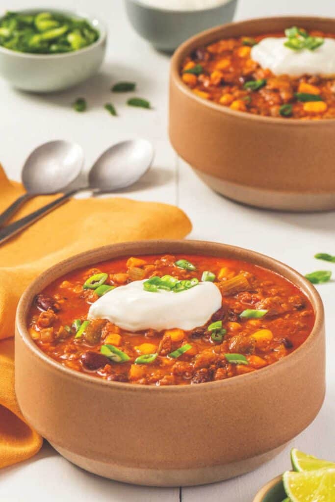 Chili con carne in a terra cotta bowl with sour cream and scallions.