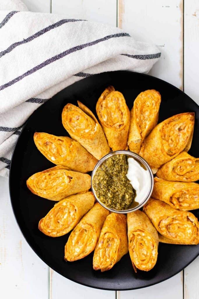 Antojitos on a black plate with a bowl in the middle with dipping sauces.