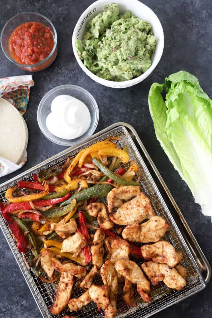 air fryer chicken fajitas with a romain lettuce head, and bowls of various toppings.