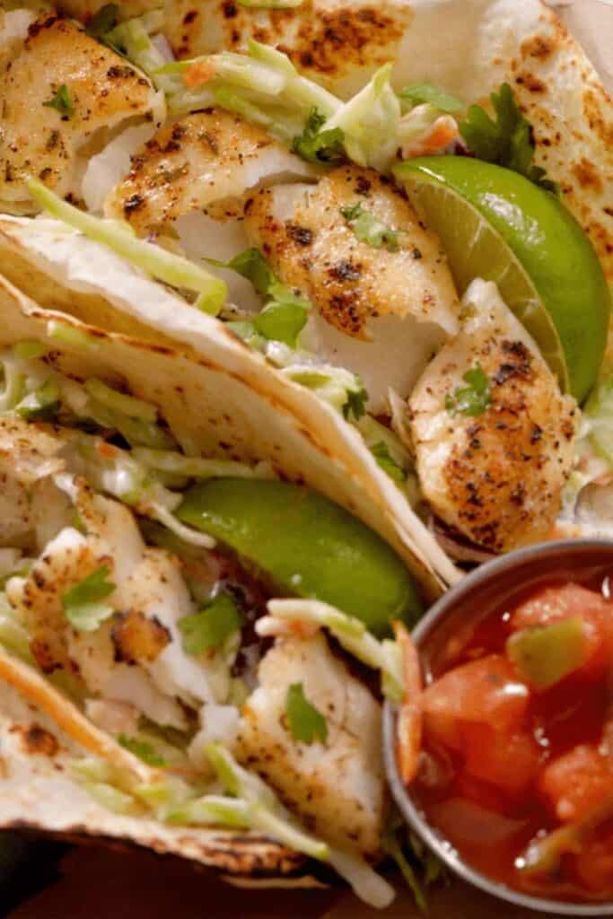 Grilled fish tacos with lime wedges and a bowl of salsa.