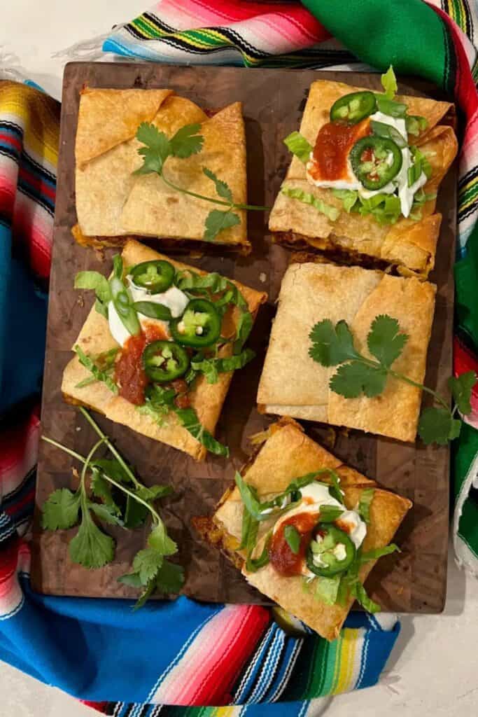 Sheet pan tacos on a wood cutting board on top of a mexican blanket.