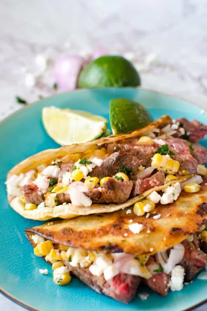 Steak Street Corn Tacos on a blue plate with lime wedges.